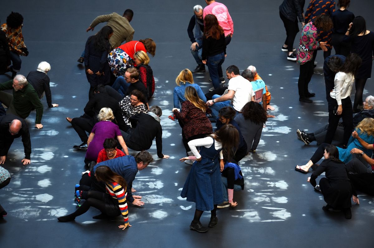 People crouching and sitting on the heat-sensitive floor in Tate Modern's Turbine Hall, leaving pale handprints where their body heat has changed the colour